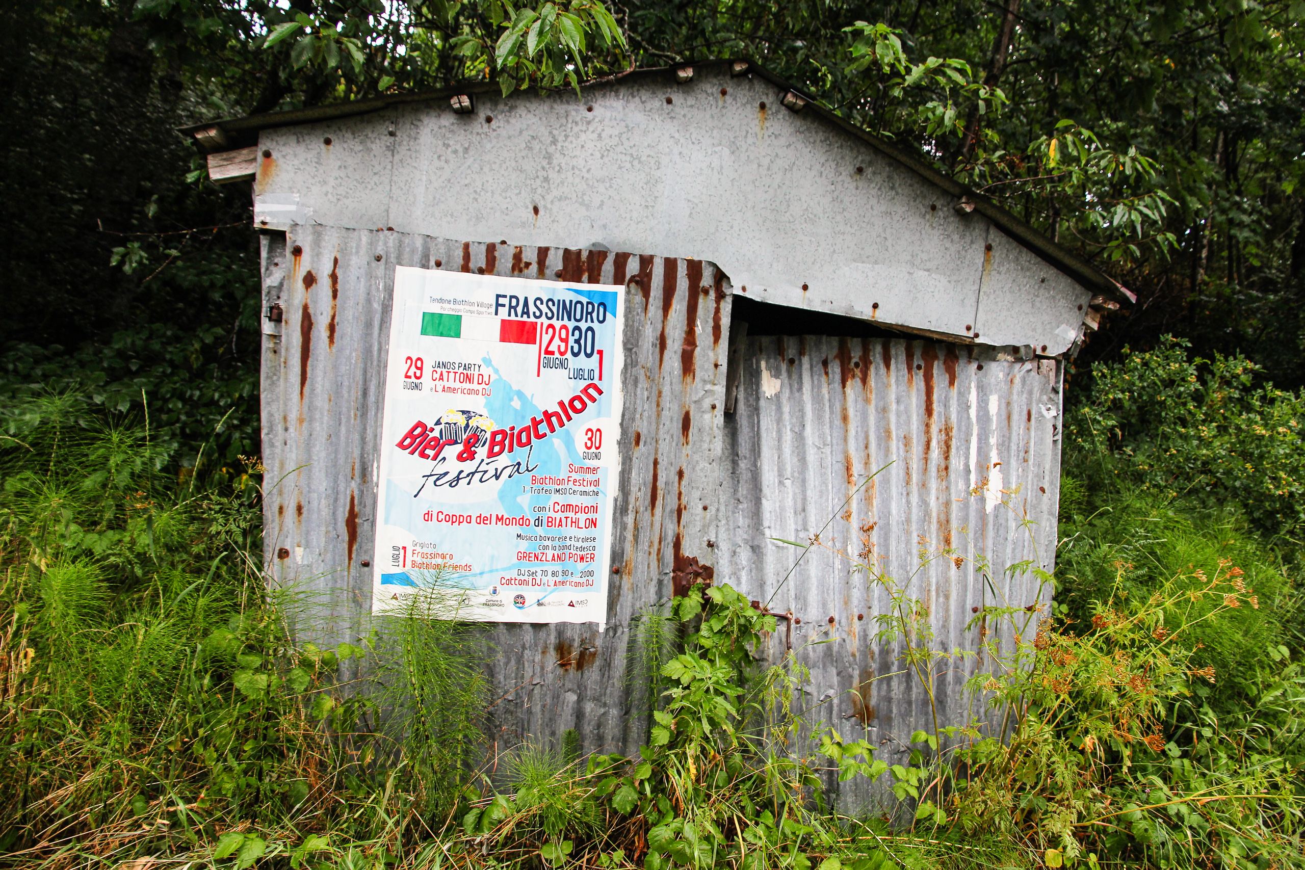 Wellblechhütte am Straßenrand, darauf das Plakat für Frassinoros „Bici & Biathlon"
